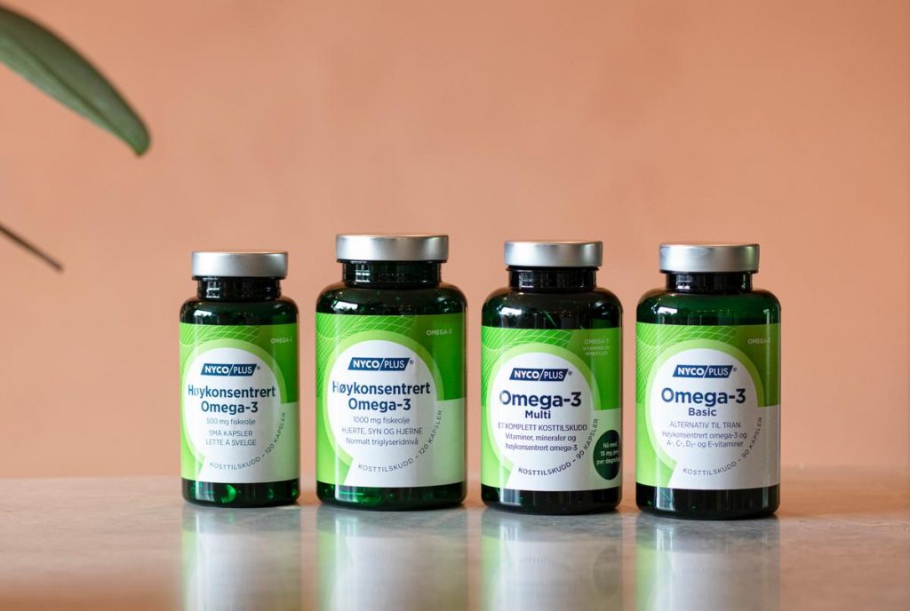 Fire ulike omega-3 produkter foran plante og ferskenfarget vegg.
