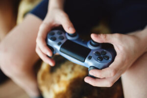En tenåring sitter på sofaen og spiller videospill. Nærbilde av hender.