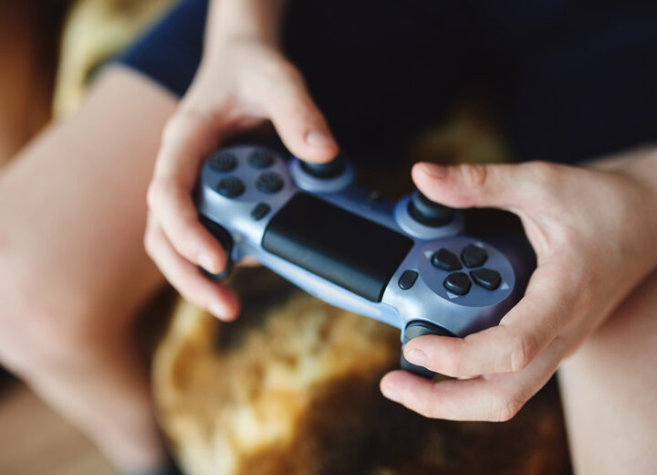 En tenåring sitter på sofaen og spiller videospill. Nærbilde av hender.
