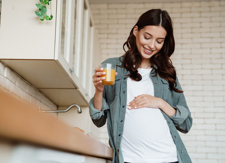Gravid kvinne holder en hånd på magen sin og drikker et glass juice
