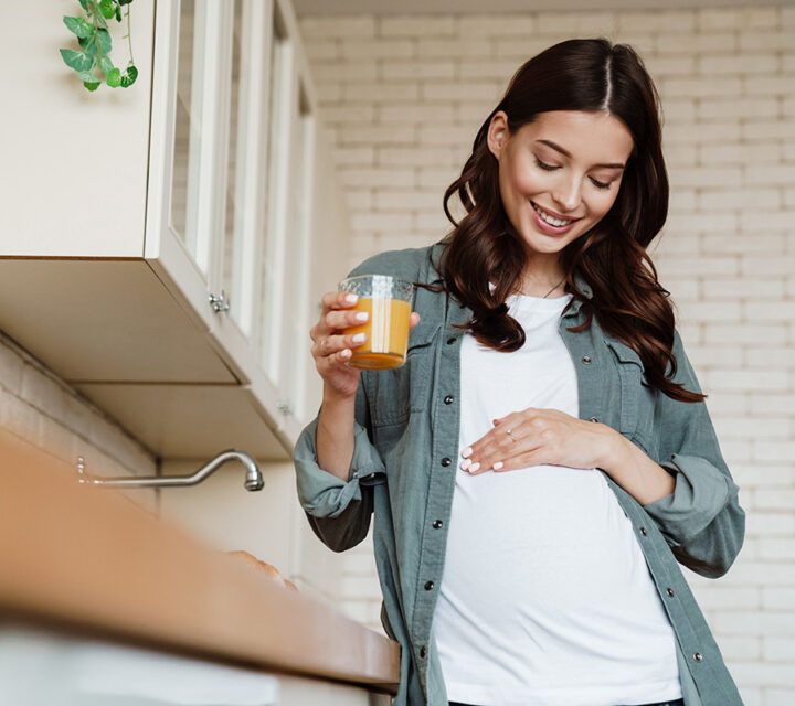 Gravid kvinne holder en hånd på magen sin og drikker et glass juice