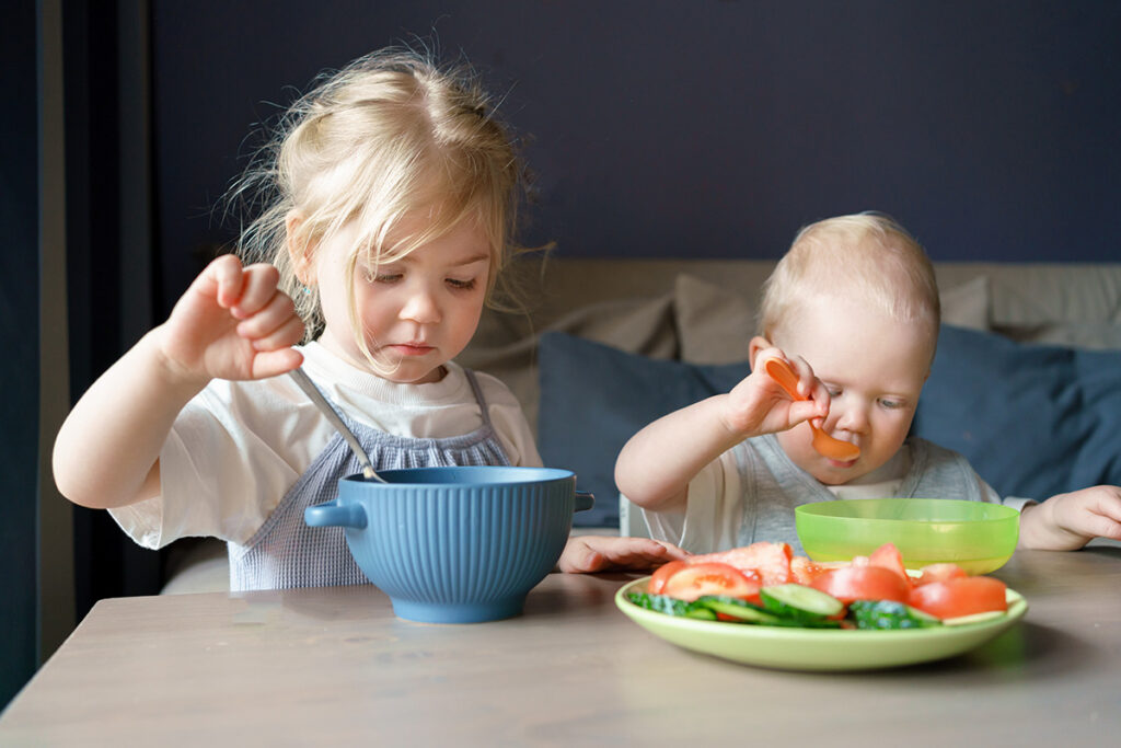 To unge barn sitter ved et bord og spiser