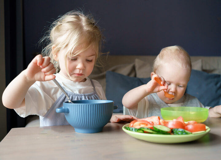 To unge barn sitter ved et bord og spiser