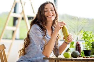Kvinne med lang hår har frukt foran seg og en juice i hendene.