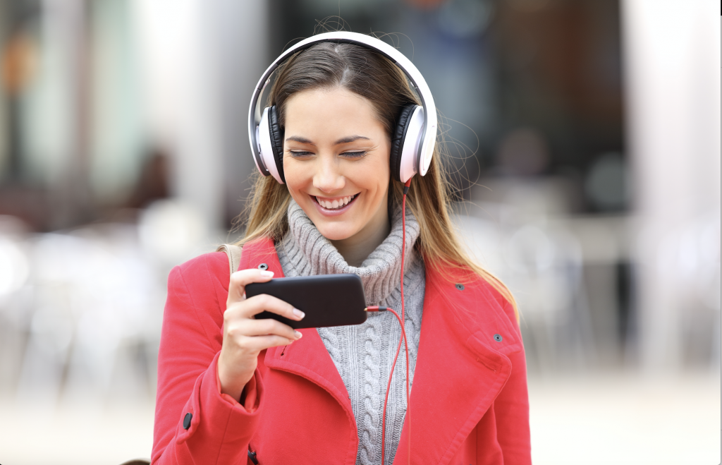 Kvinne i rød kåpe med headset som ser på noe på mobilen