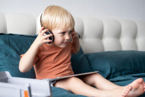 Et barn sitter i en sofa med nettbrett og hodetelefoner