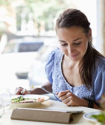 Kvinne spiser en sunn lunsj og ser ned på ipaden sin