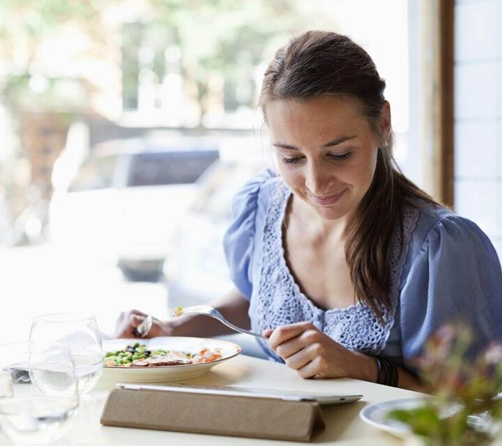 Kvinne spiser en sunn lunsj og ser ned på ipaden sin