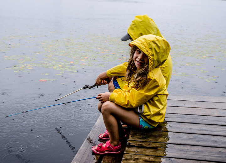 To barn som sitter på en brygge i regnet og fisker