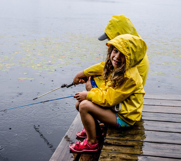 To barn som sitter på en brygge i regnet og fisker