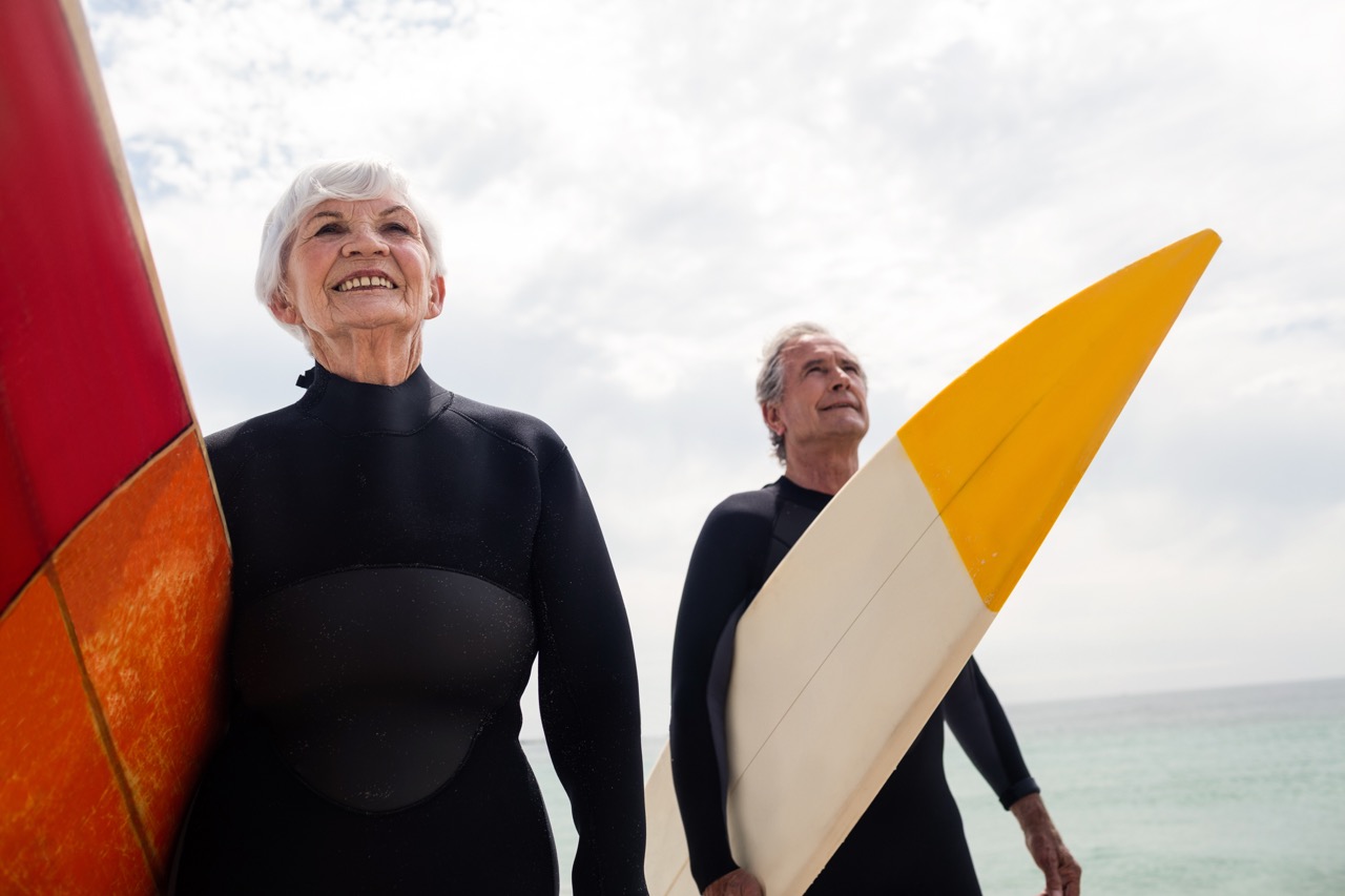 Senior couple in wetsuit holding surfboard on beach on a sunny day