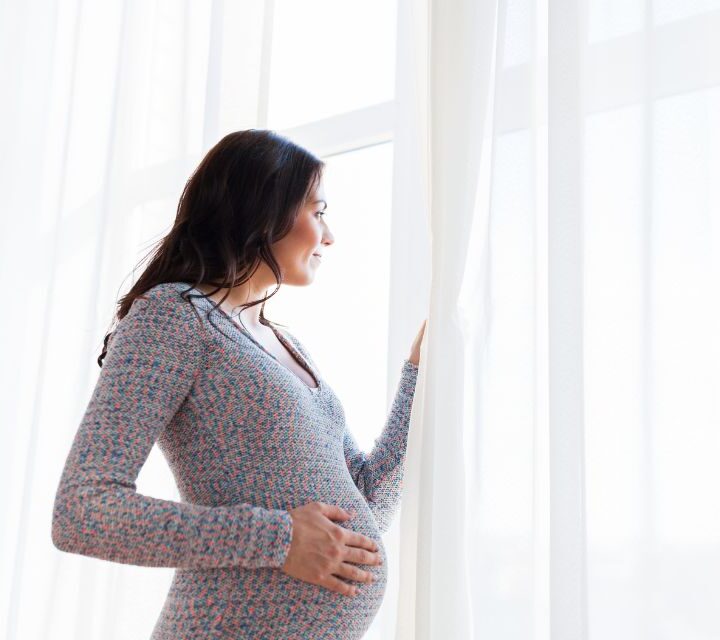 Gravid kvinne ser ut av vinduet