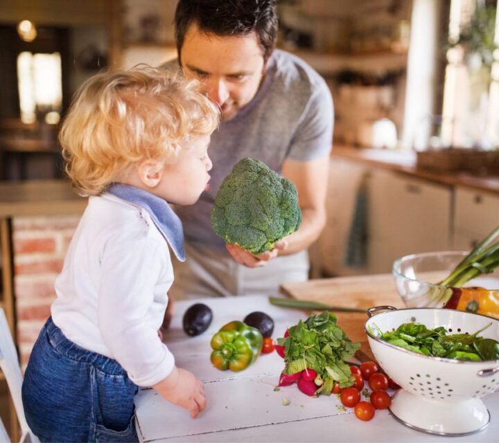 Barn og mann som står ved spisebord fullt av grønnsaker.